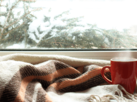 blanket and warm mug next to a window inside a home